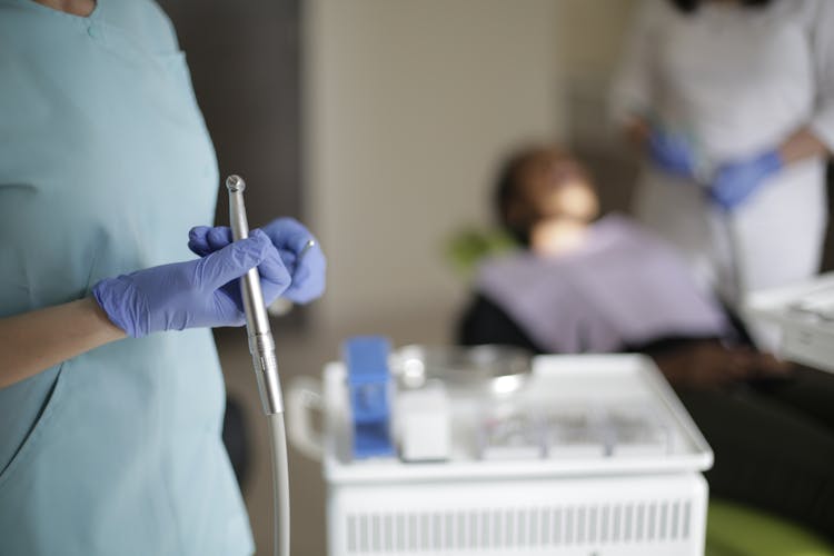 Crop Dentist Holding Dental Drill For Treating Teeth Of Patient