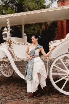 Stylish woman in chic white dress poses beside a vintage horse carriage in Leon, Mexico.