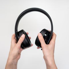 Hands holding a pair of black wireless headphones