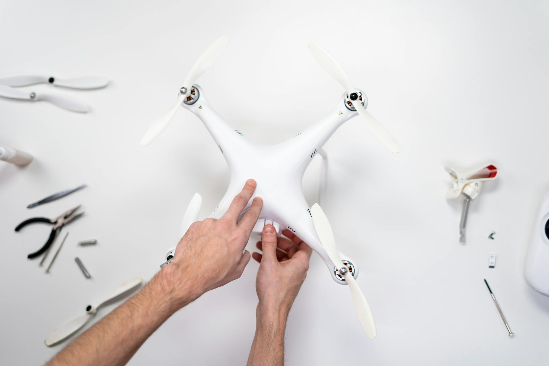 Close-up photo of hands assembling a white drone with tools on a table.