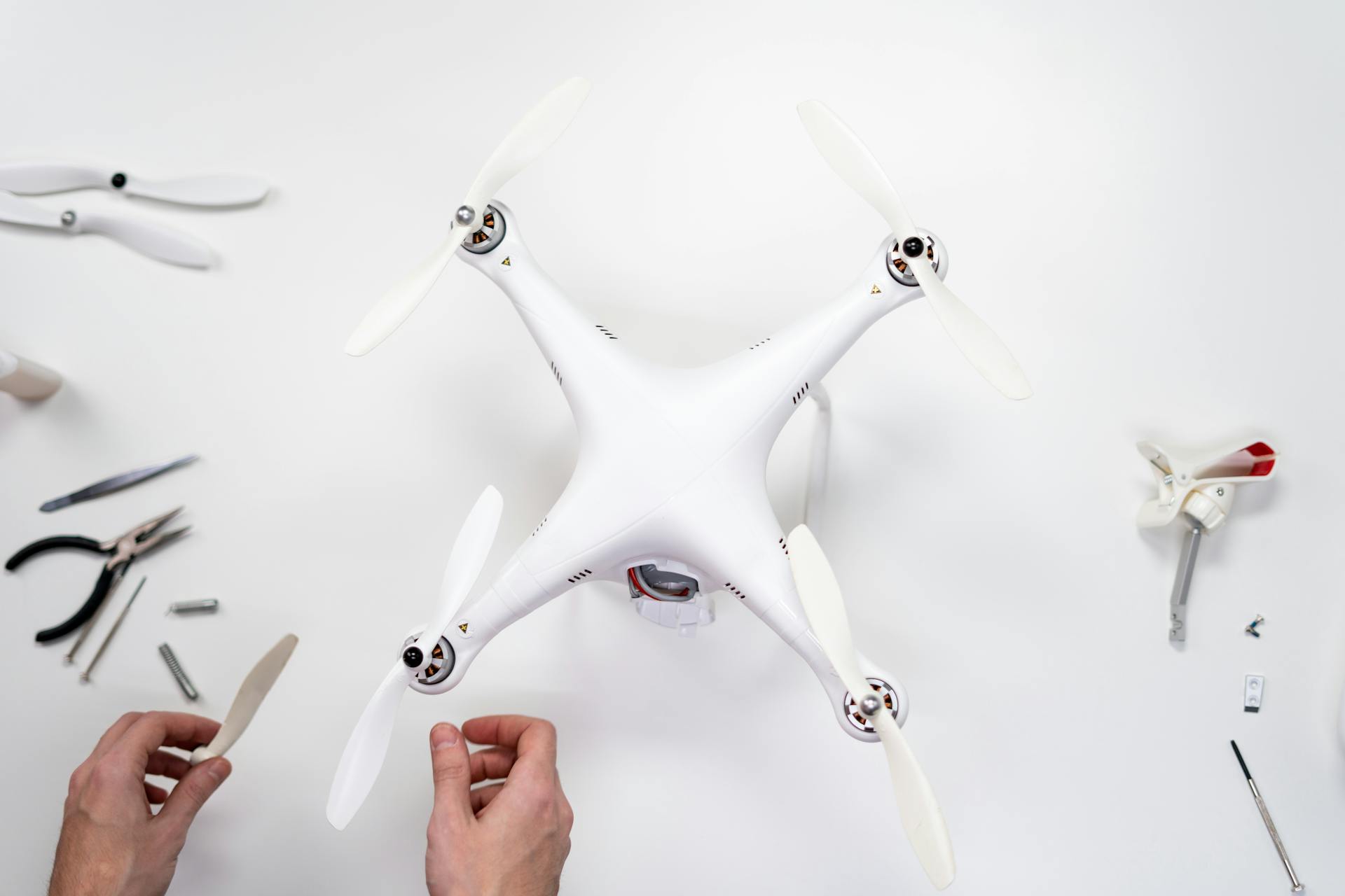 Hands assembling a quadcopter drone on a white surface with various tools around.