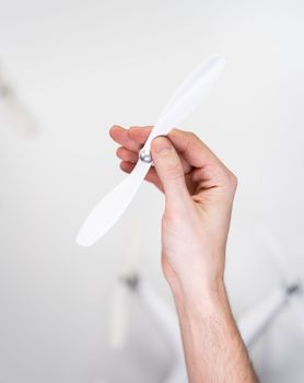 A hand holding a white drone propeller against a blurred background, emphasizing drone technology.