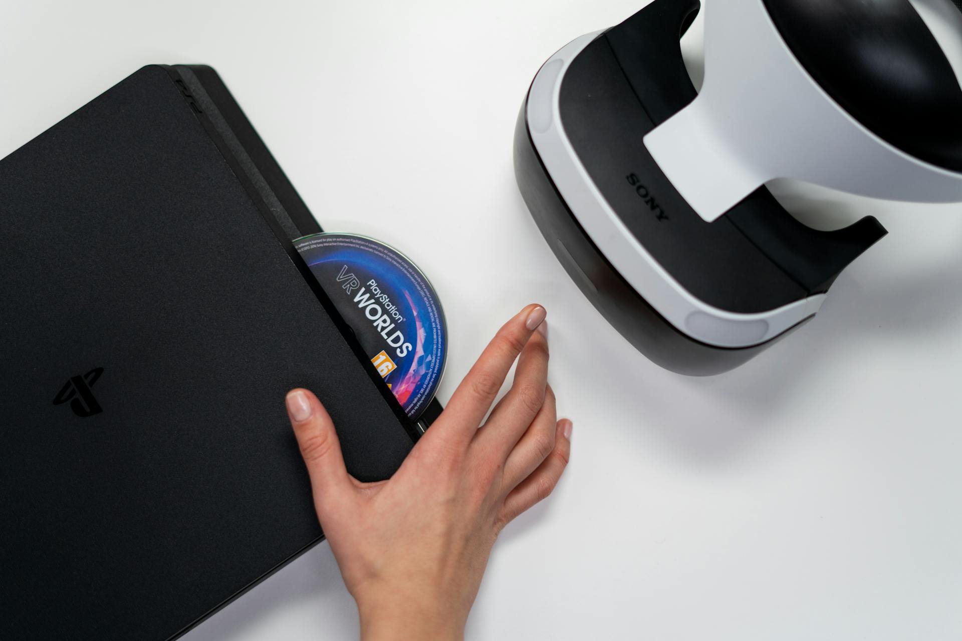 Close-up of a hand inserting a VR World's disc into a PlayStation with VR headset nearby.