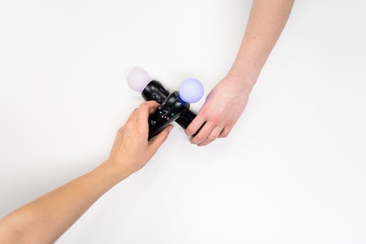 Two hands holding a black gaming controller with glowing spheres, flat lay.
