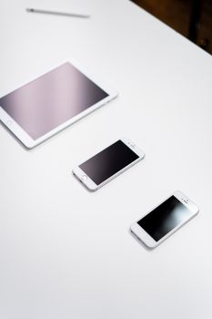 Overhead view of a digital tablet, smartphone, and stylus on a white surface.