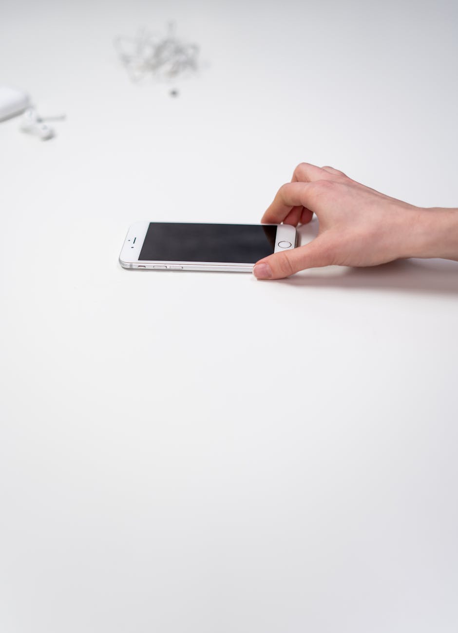 Minimalist composition of a hand holding a smartphone over a white surface, emphasizing modern technology. refurbished iPhones and e-waste