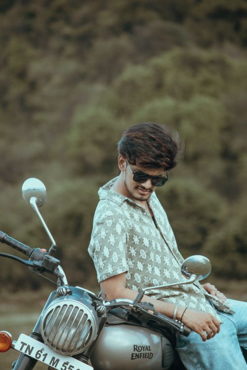 Free Stylish young man on Royal Enfield motorcycle outdoors near forest. Stock Photo