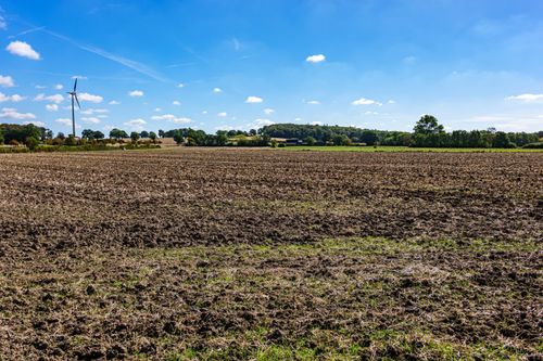Free Wide-angle view of a plowed field under clear blue skies with a wind turbine in the distance. Stock Photo