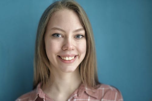 Free Cheerful blond haired blue eyed lady in casual wear toothy smiling at camera while standing against blue background Stock Photo