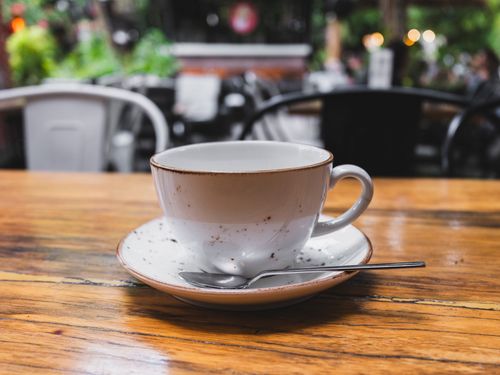 Free A rustic ceramic coffee cup with saucer on a wooden table in a café setting. Stock Photo