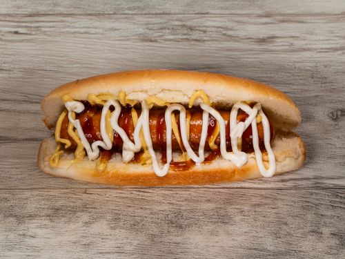 Free A delicious hotdog topped with ketchup, mustard, and mayonnaise on a rustic wooden table. Stock Photo
