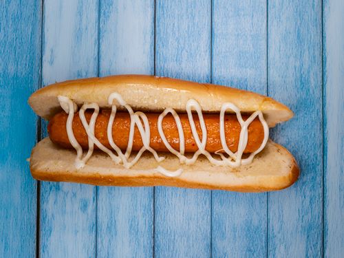 Free Delicious hotdog drizzled with mayonnaise served on a rustic blue wooden table. Stock Photo