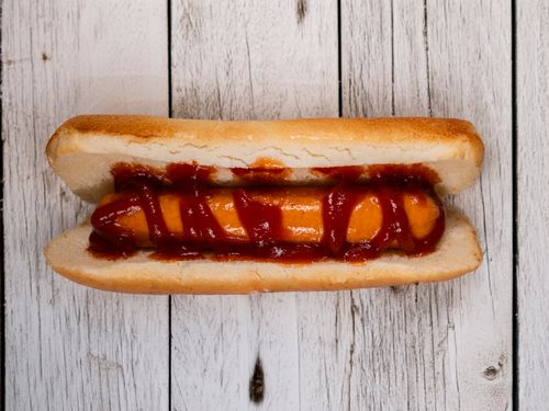 Free A mouthwatering hotdog topped with ketchup on a rustic wooden table, capturing the essence of comfort food. Stock Photo