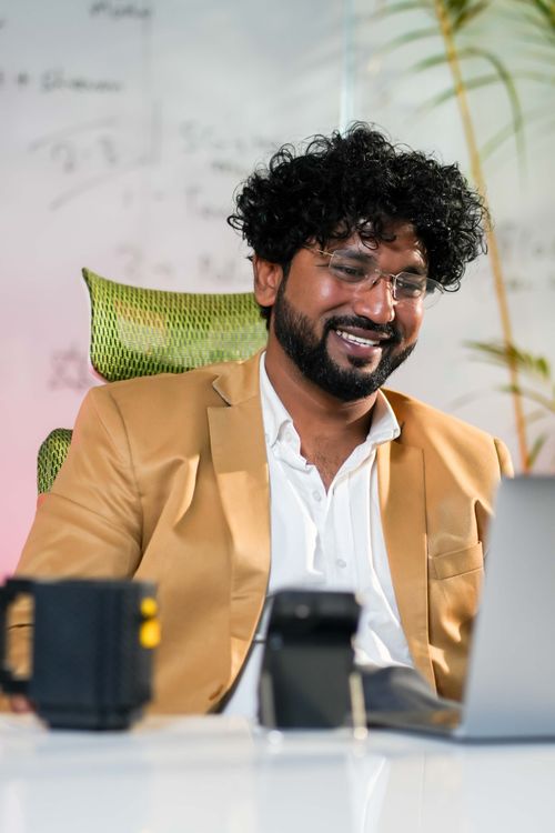 Free Smiling young professional in a smart blazer, engaging in a video call from a modern workspace. Stock Photo