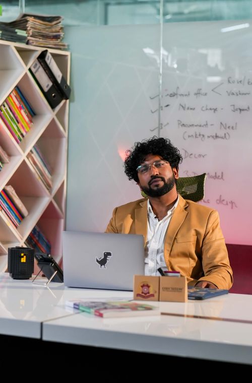 Free Confident businessman sitting at a desk in a modern office with bookshelves and a whiteboard. Stock Photo