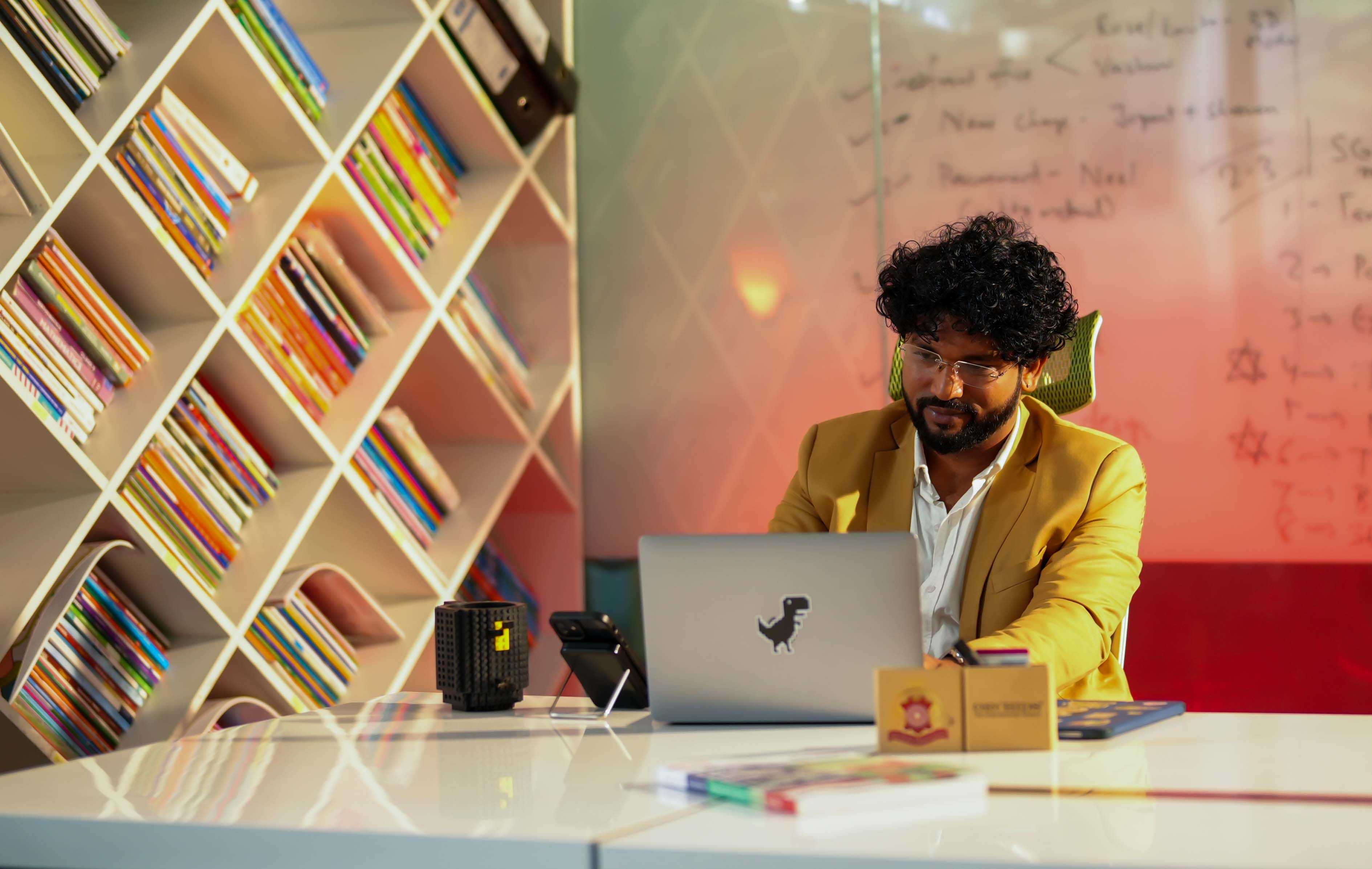 Professional working on a laptop in a stylish office with colorful bookshelves and sleek design.