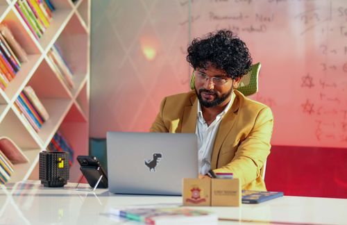 Free Man in a cozy office working on a laptop, surrounded by books and a creative environment. Stock Photo