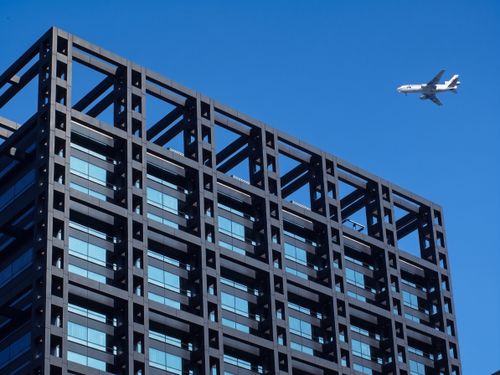 Free A minimalist shot of a building with an airplane in the blue sky. Stock Photo
