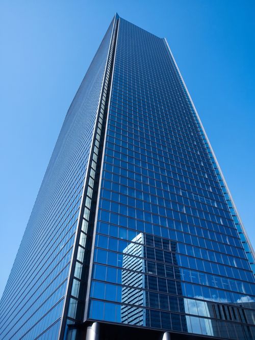 Free A sleek modern skyscraper towers into a vibrant blue sky, reflecting nearby structures. Stock Photo