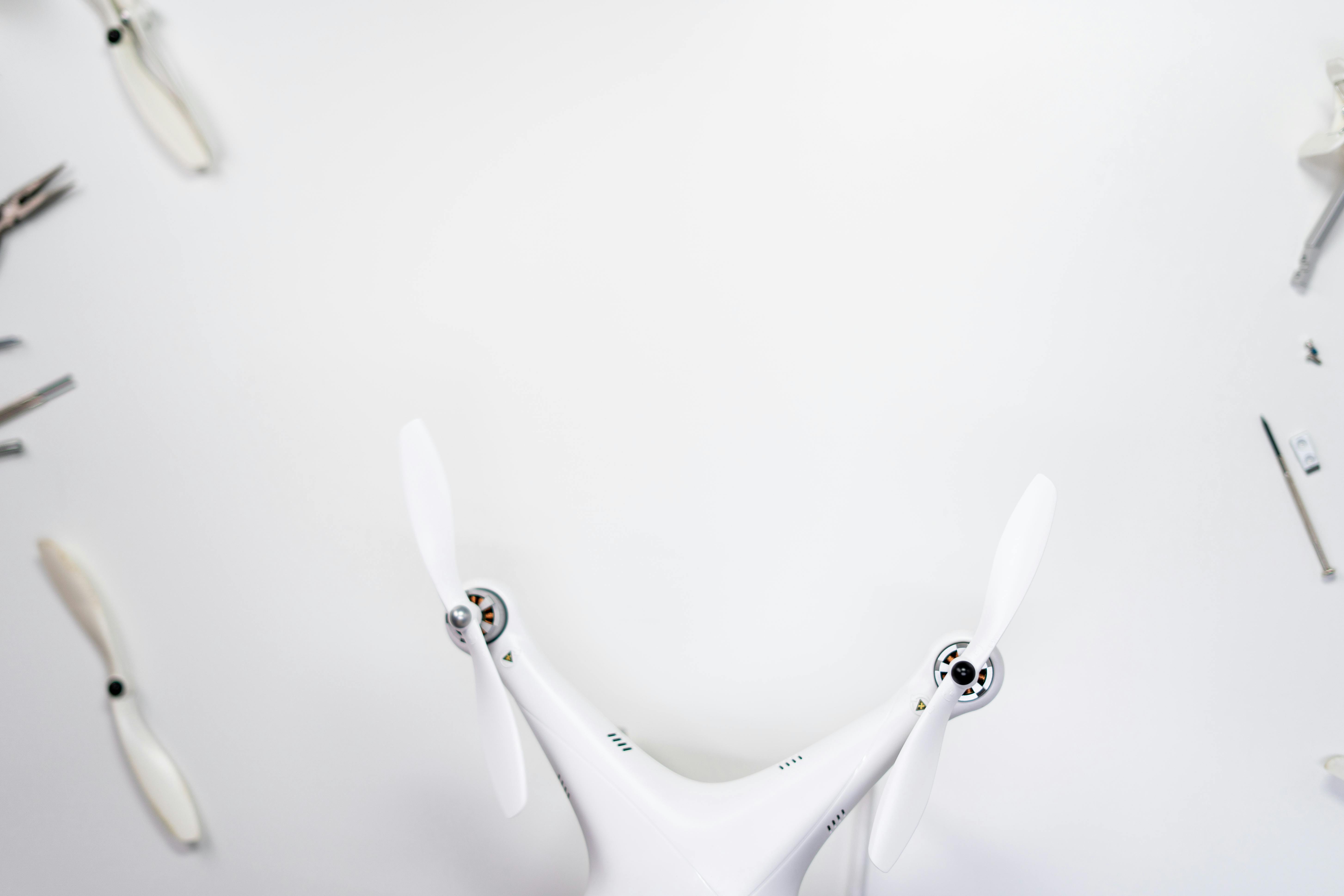 Top-down view of a white quadcopter drone with tools on a white background.