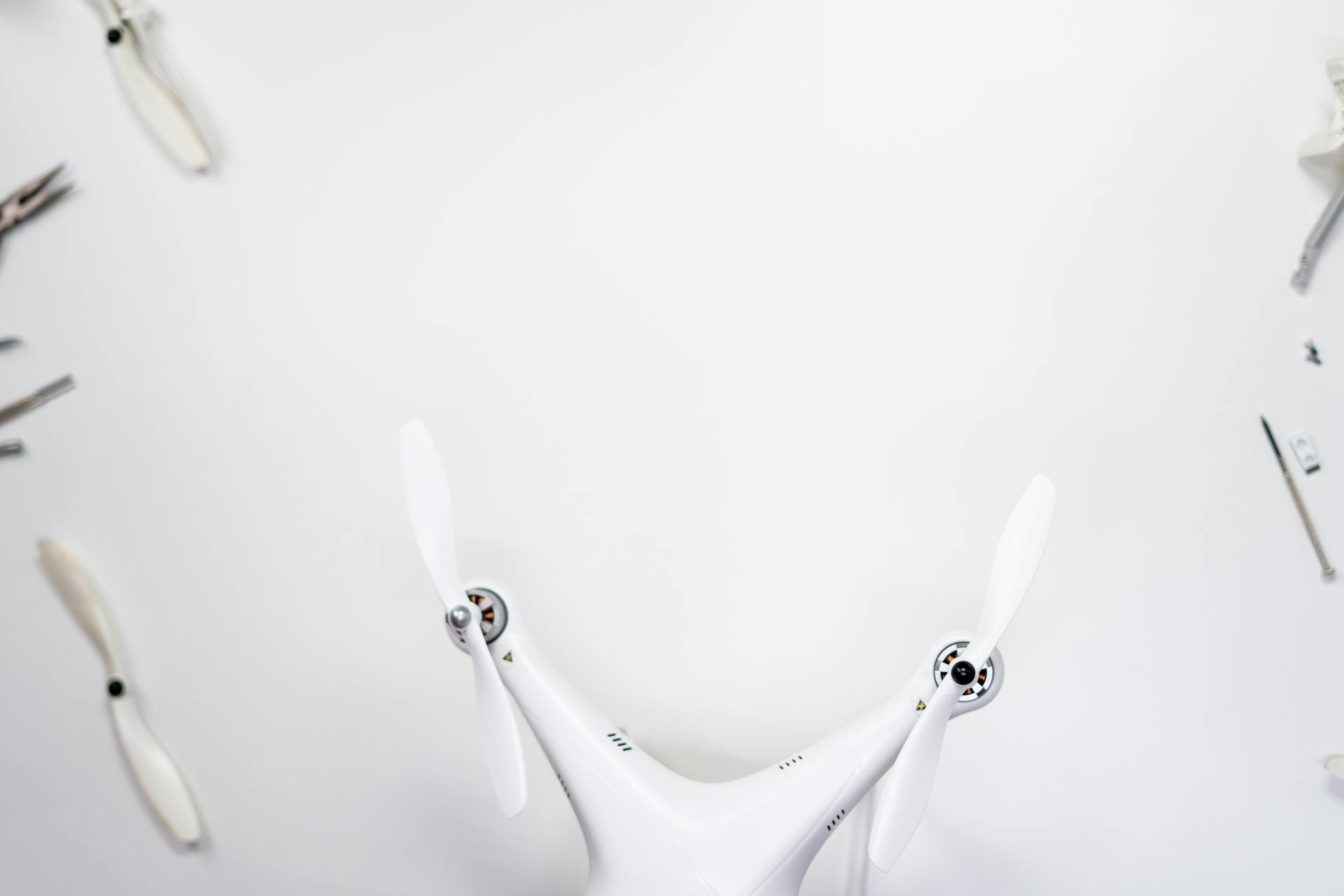 Top-down view of a white quadcopter drone with tools on a white background.