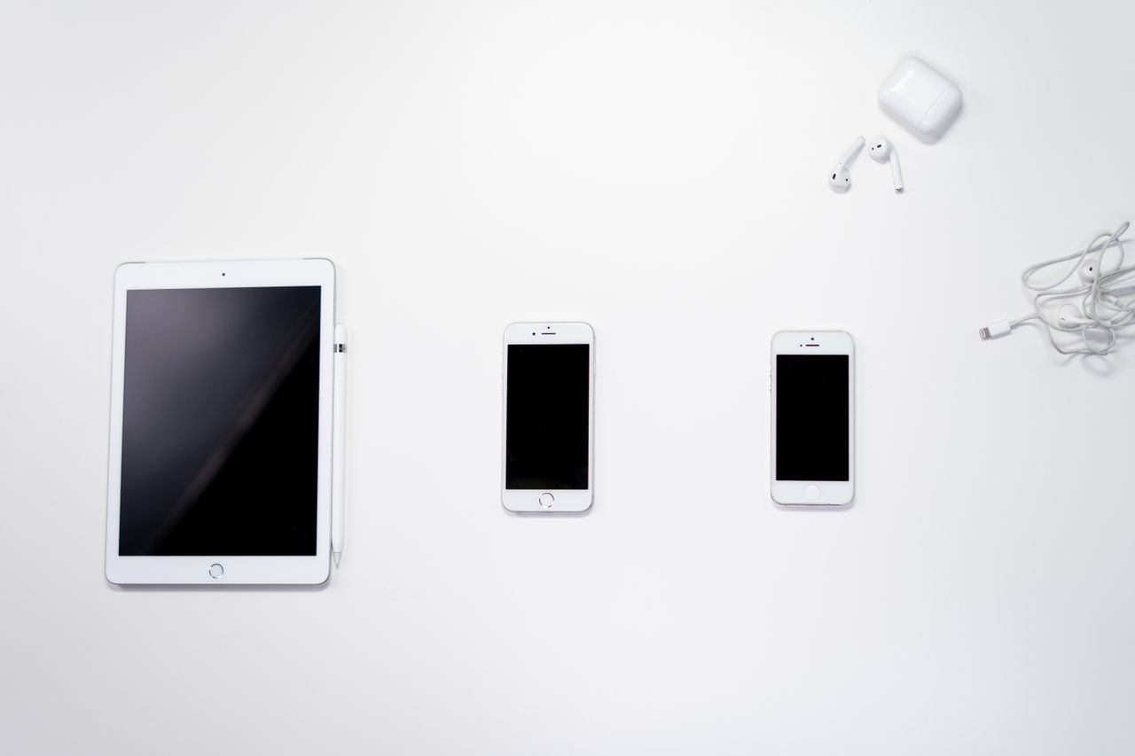 flat lay of smartphone tablet and earphones arranged on a white surfac
