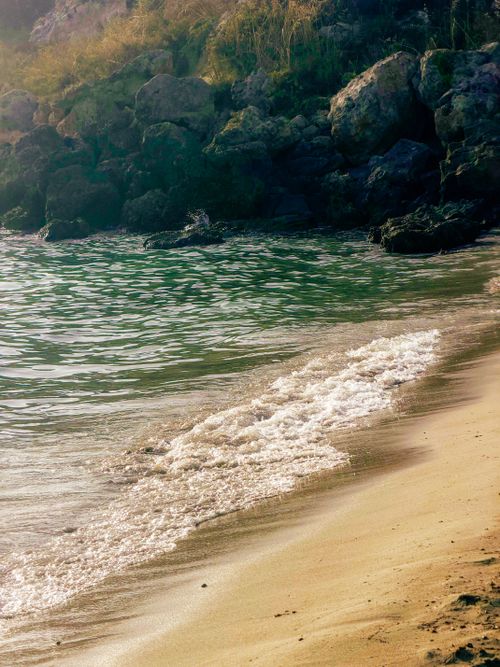 Free Calm beach scene with rocks and gentle waves in soft sunlight. Stock Photo