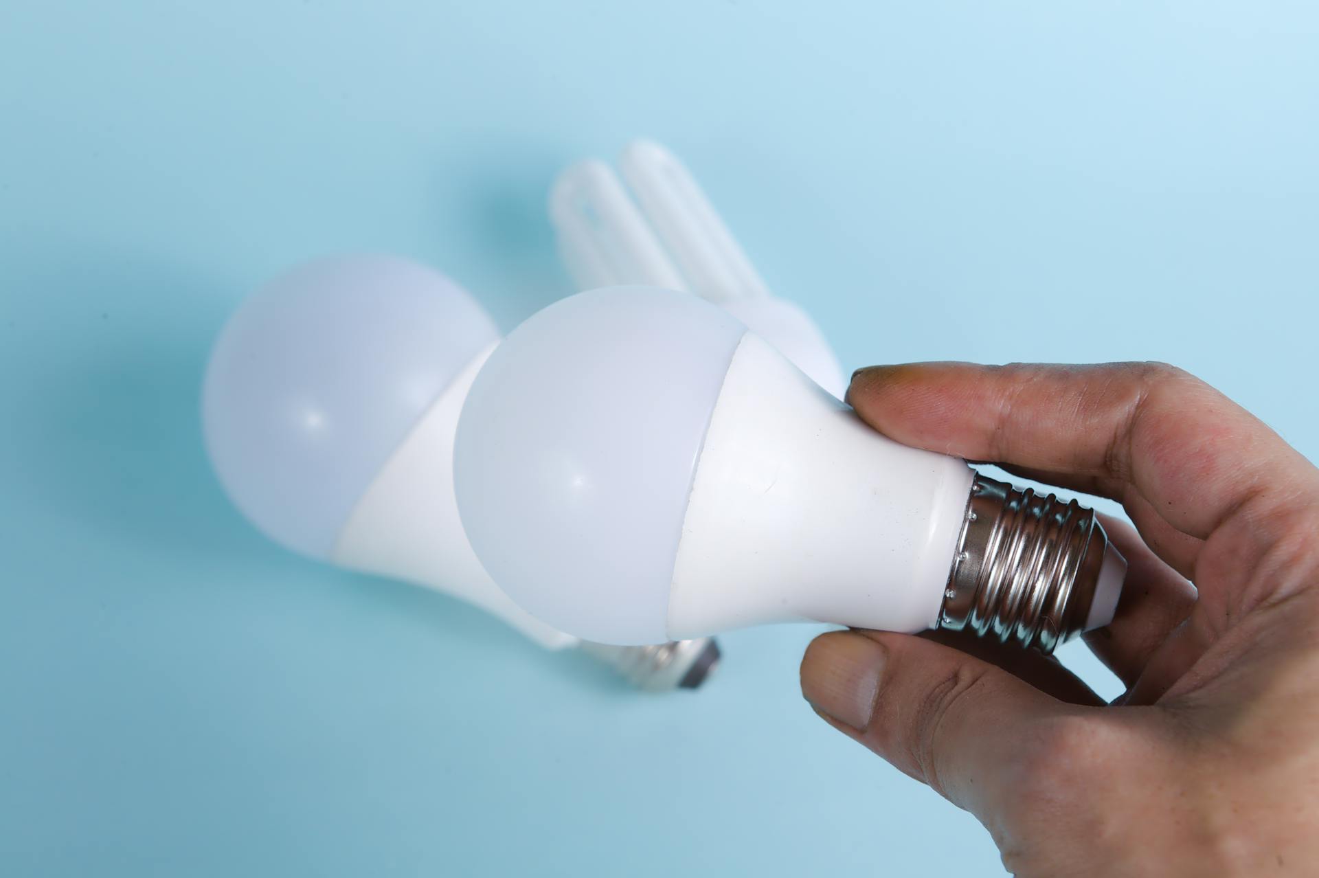 Close-up of hand holding energy-efficient LED light bulbs on a blue background.