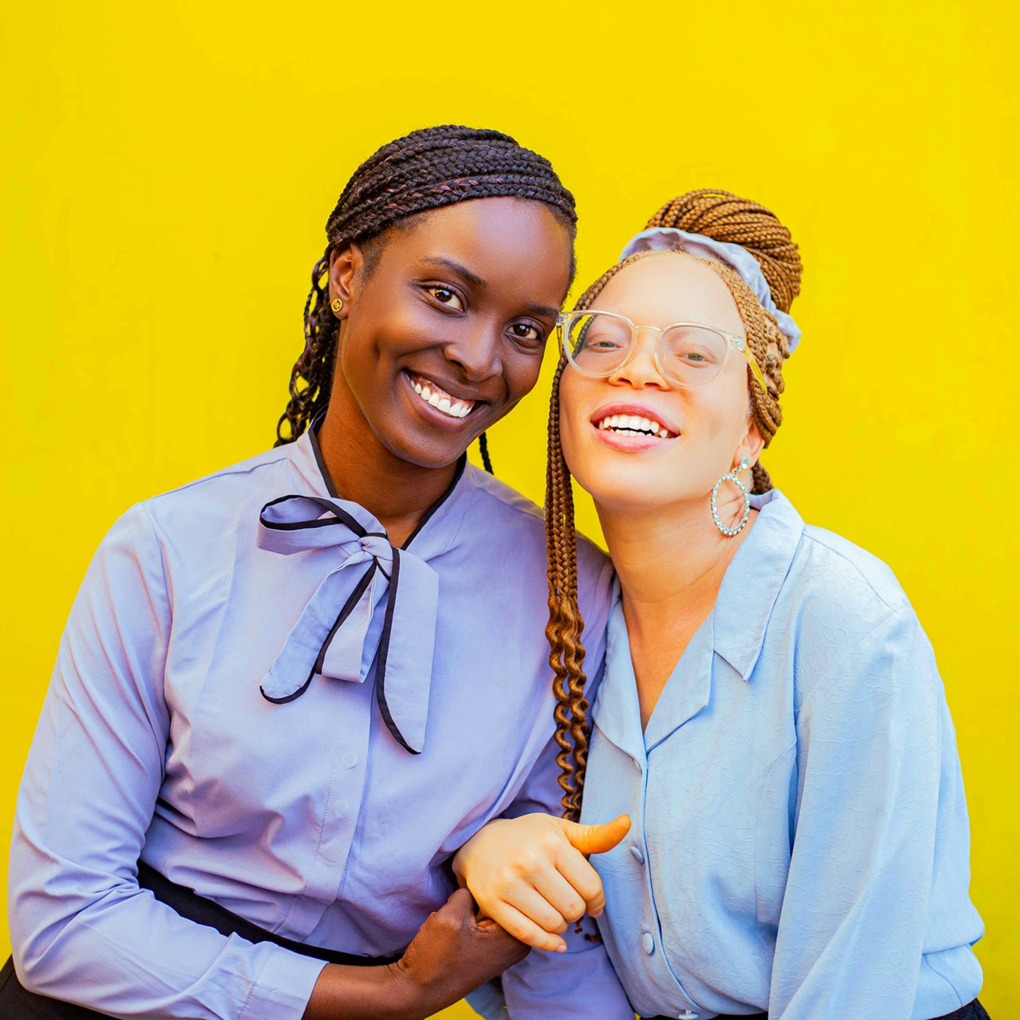 Two diverse friends smiling warmly against a vibrant yellow background.