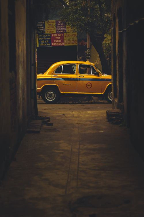 Free Yellow vintage taxi seen through a narrow alleyway, conveying urban nostalgia. Stock Photo