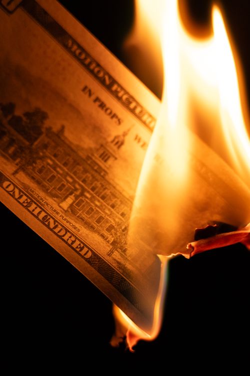 Free A hundred dollar bill igniting in flames against a dark background, symbolizing financial waste. Stock Photo