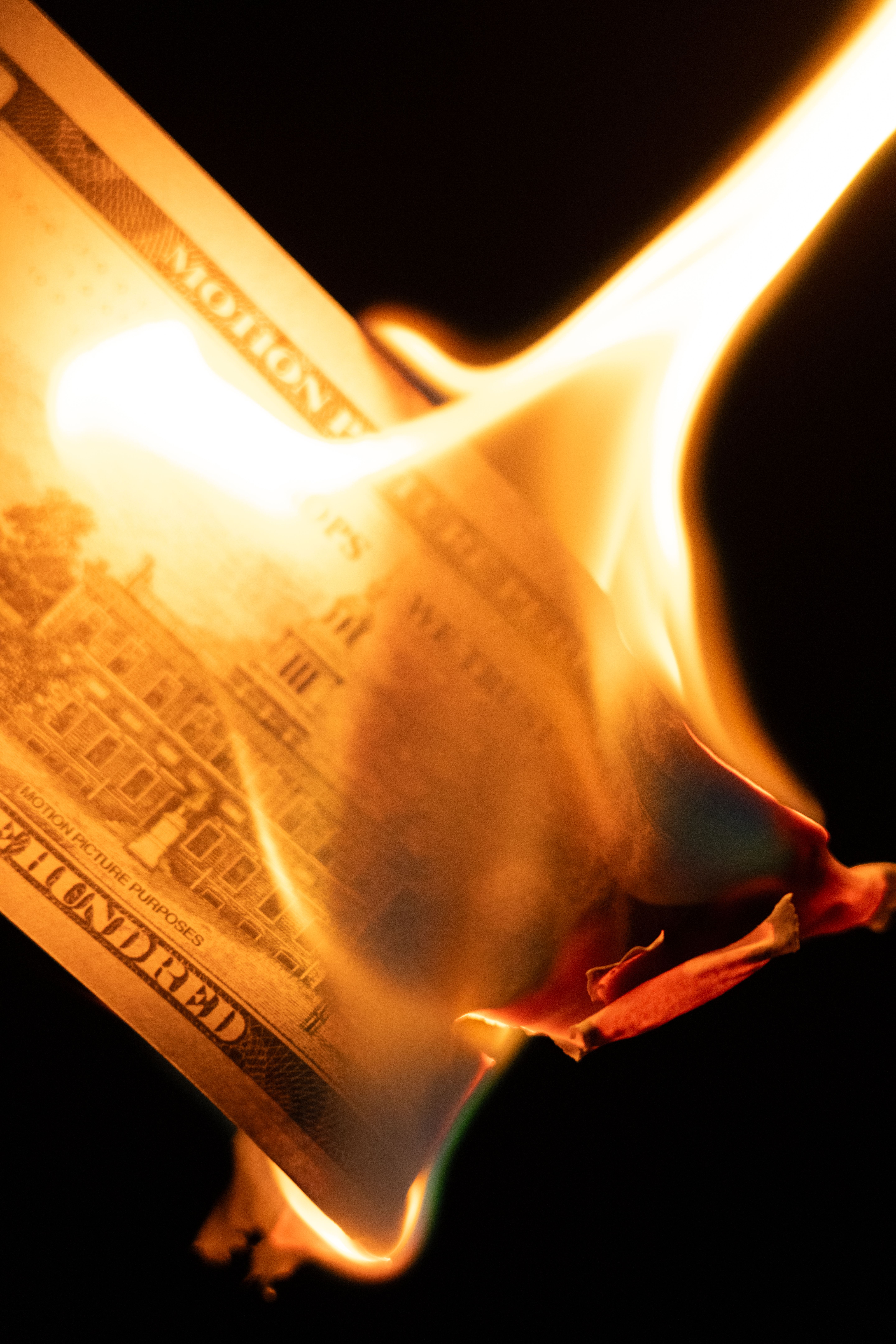 A close-up of a burning hundred dollar bill against a black background, symbolizing loss or waste.