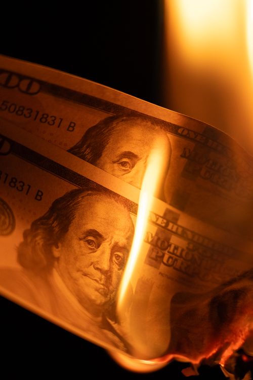 Free Close-up of a burning hundred dollar bill with intense lighting, representing financial loss. Stock Photo