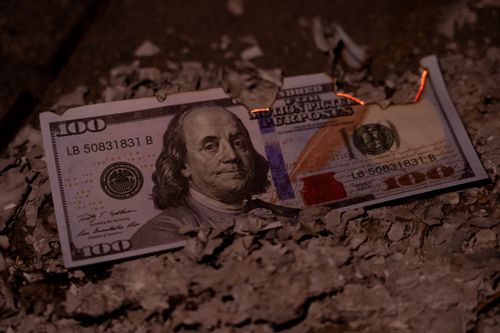 Free A burning hundred dollar bill amidst ashes, symbolizing economic loss. Stock Photo
