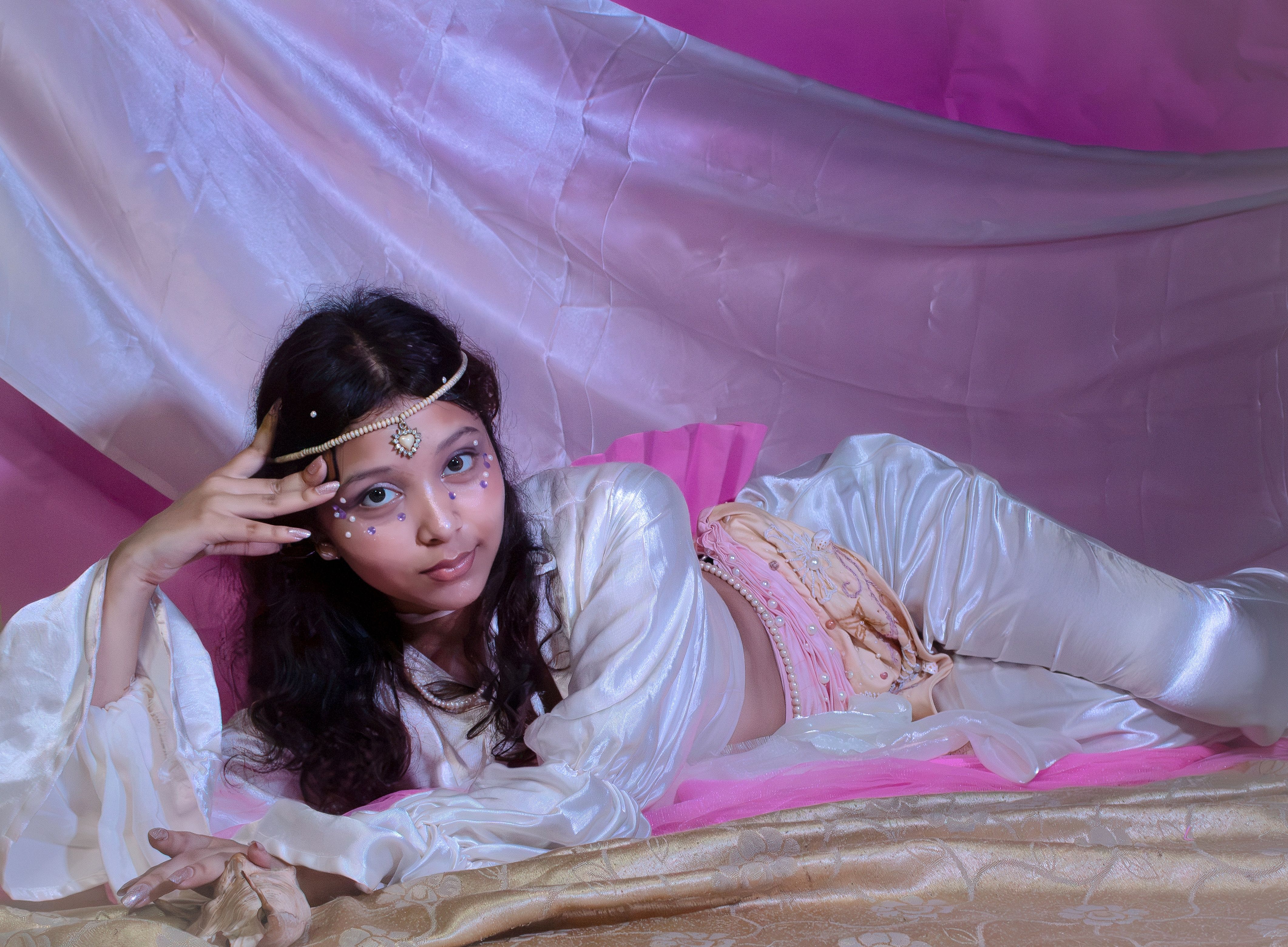 A woman dressed in elegant, oriental-inspired attire posed gracefully on silk drapes.