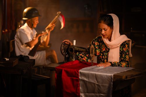 Free A woman sews with an antique machine, soldier behind, in Indonesia. Stock Photo