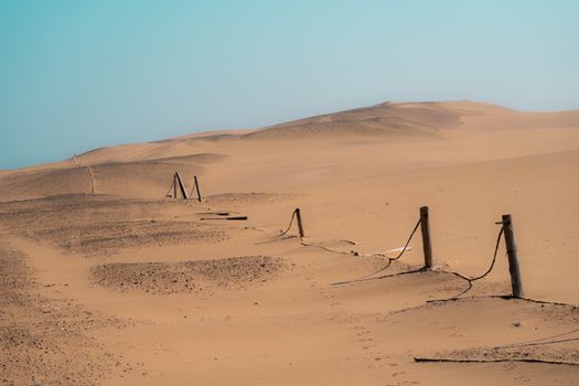 Expansive view of Namib Desert dunes and a rustic fence in Swakopmund, Namibia.