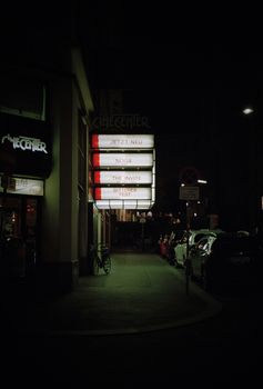Moody nighttime view of an urban cinema street with neon signs.