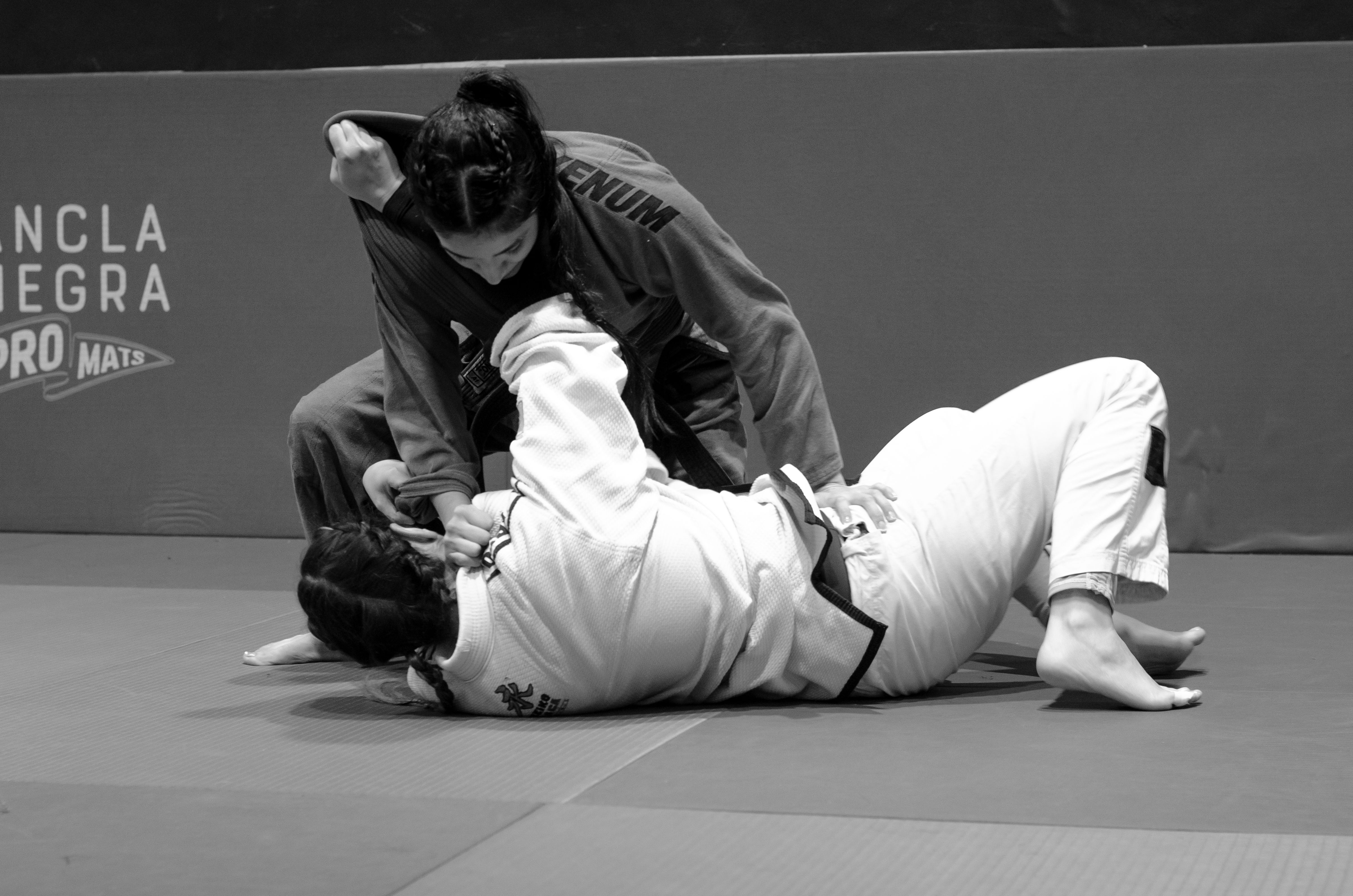 Two women engage in Brazilian Jiu Jitsu training, showcasing technique and skill.