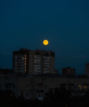 A full moon illuminating city buildings in a nighttime skyline view.