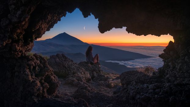 Sitting in cave watching twilight mountain scenery above sea of clouds