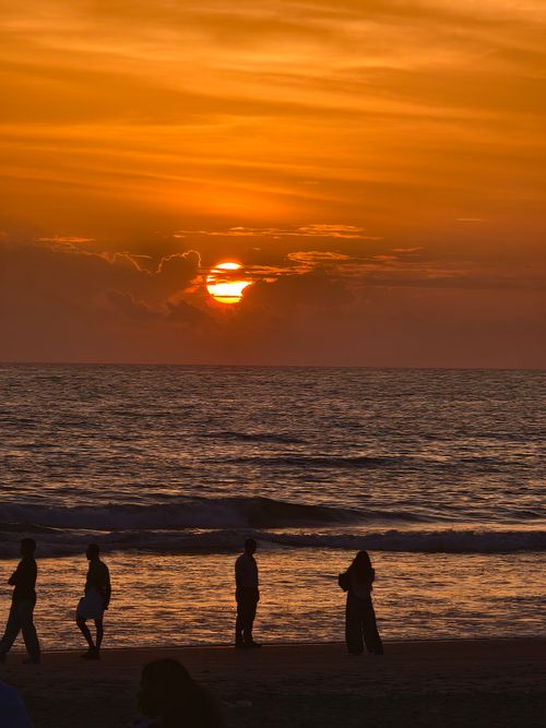 Free Silhouetted figures walking along a beach at sunset with stunning orange sky. Stock Photo