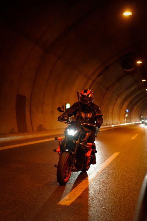 Free Motorcyclist wearing gear rides through a lit tunnel at night, showcasing adventure and speed. Stock Photo