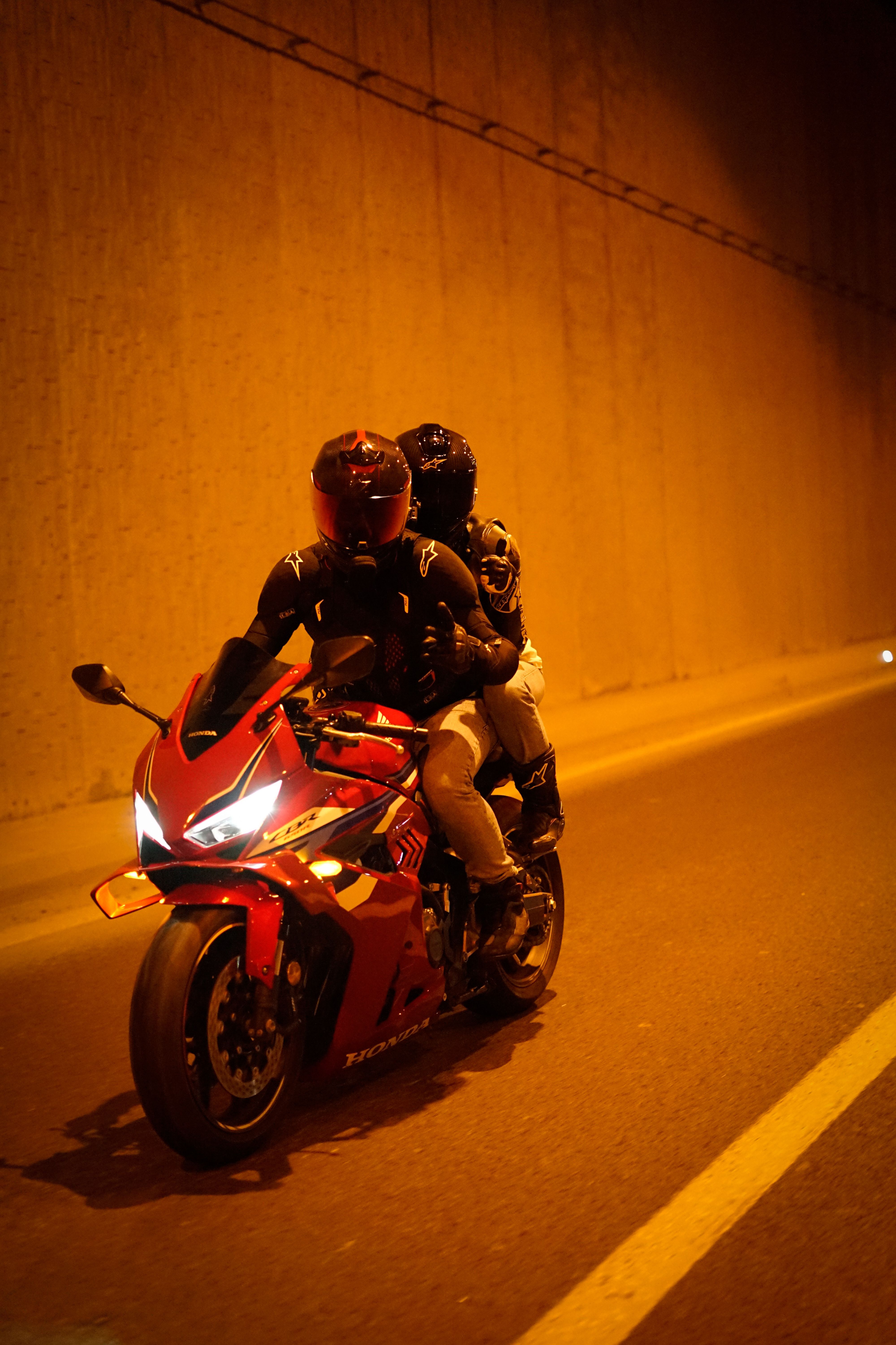 Two people riding a red motorcycle through an illuminated tunnel at night.