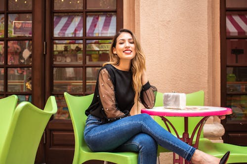 Woman In Black Long Sleeve Top And Blue Denim Jeans Sitting On Green Chair