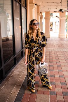 一名女子身着充满活力的几何图案连身裤，戴着太阳镜，在户外摆出时尚的姿势