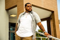 一名有纹身的时尚男子自信地在一栋现代建筑附近摆姿势