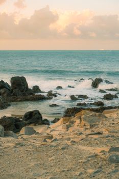 Peaceful coastal scene with rocks and waves under a pastel sunset sky in RN, Brazil.