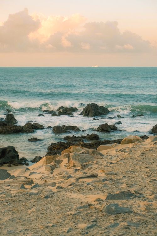 Free Peaceful view of a sandy beach with rocky shorelines and calm sea at sunset in Natal, Brazil. Stock Photo
