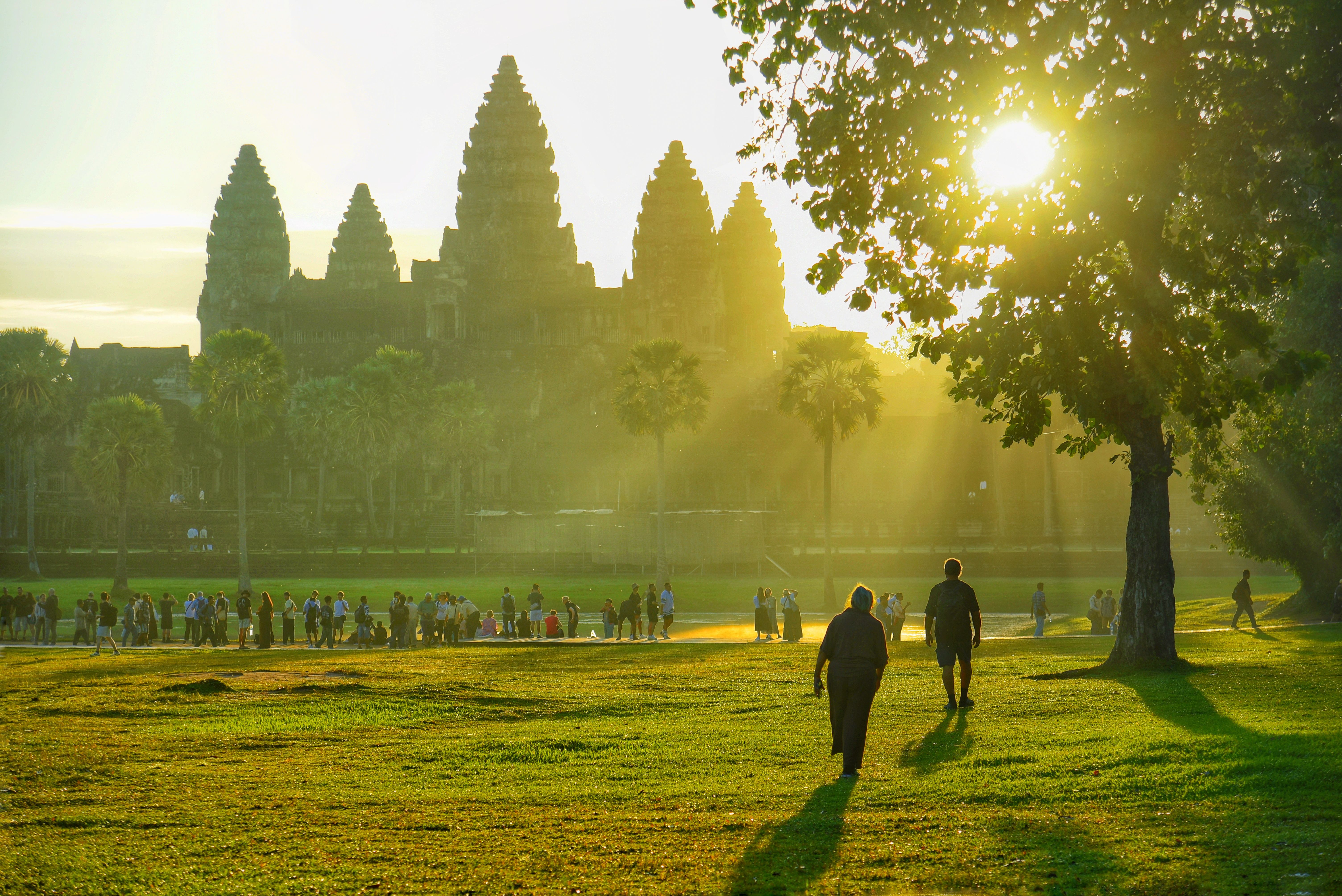 Tourists exploring Angkor Wat as the sun rises, casting golden light through the trees.